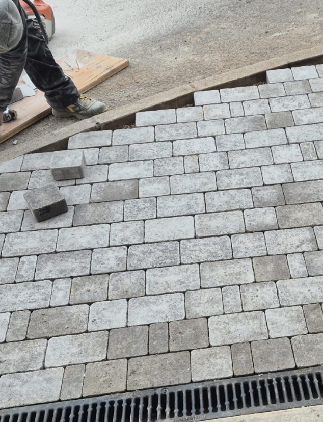Un ouvrier du bâtiment pose des pavés sur une surface courbe, à proximité d'un drain.