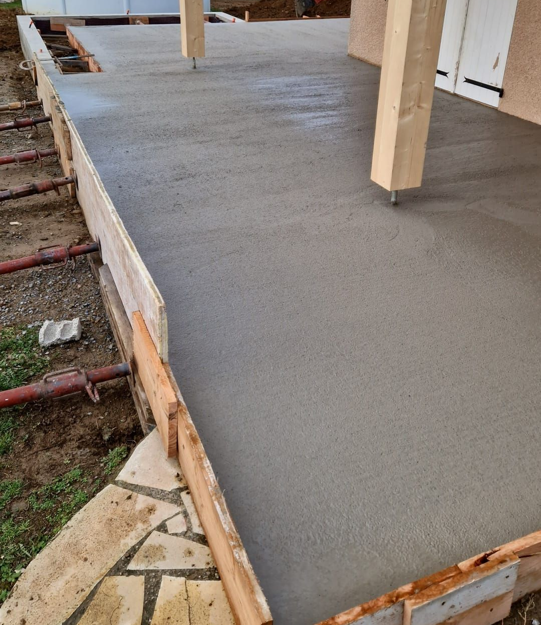 Terrasse en béton fraîchement coulé avec structure en bois et poutres de soutien.