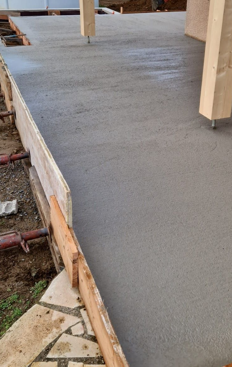 Terrasse en béton fraîchement coulé avec bordures en bois et colonnes de soutien en bois.