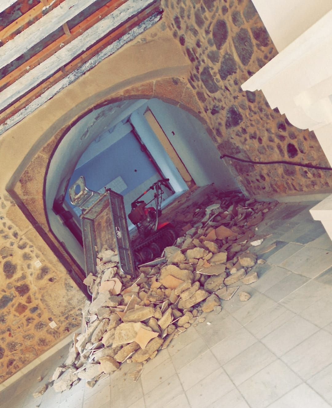 Arche en pierre effondrée et décombres à l'intérieur d'un bâtiment aux murs de pierre et aux poutres en bois.