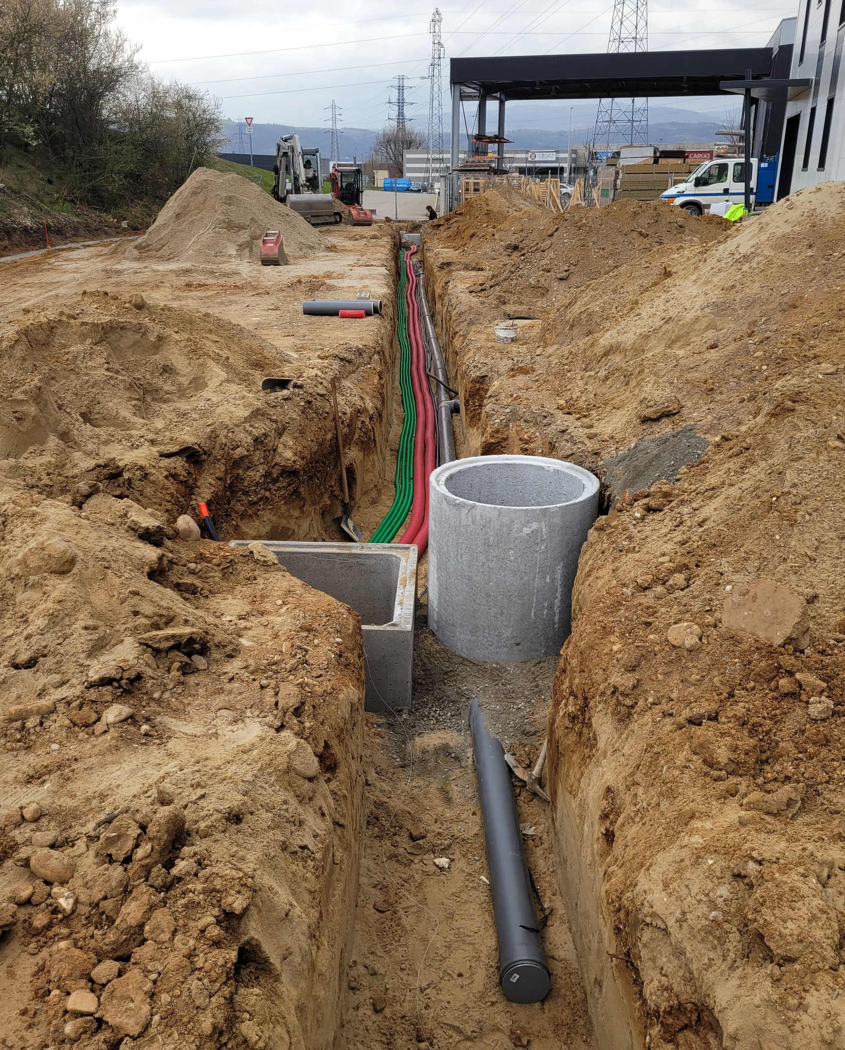 Des conduits ondulés rouges, enroulés et empilés, avec d'autres tuyaux sur un chantier de construction.