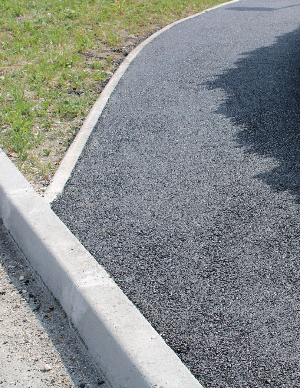 Allée asphaltée avec bordure en béton, jouxtant pelouse et terre.
