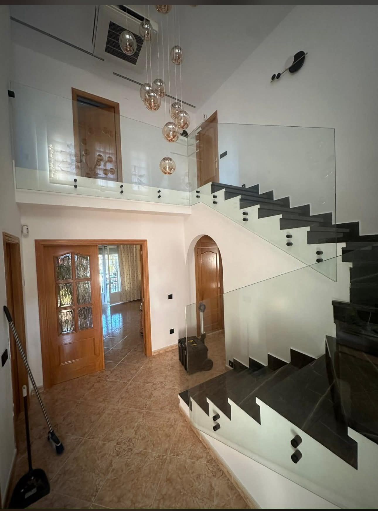 Interior moderno con escalera, barandillas de vidrio y múltiples puertas en un espacio bien iluminado y de paredes blancas.