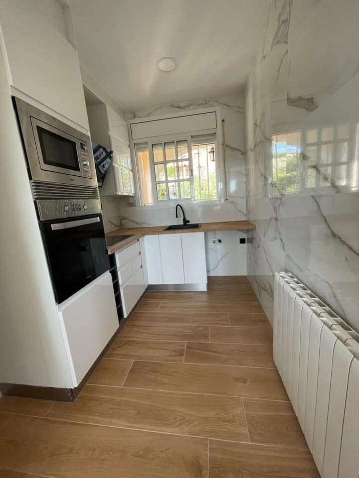 Cocina moderna con gabinetes blancos, piso imitación madera y pared imitación mármol. Electrodomésticos de acero inoxidable.