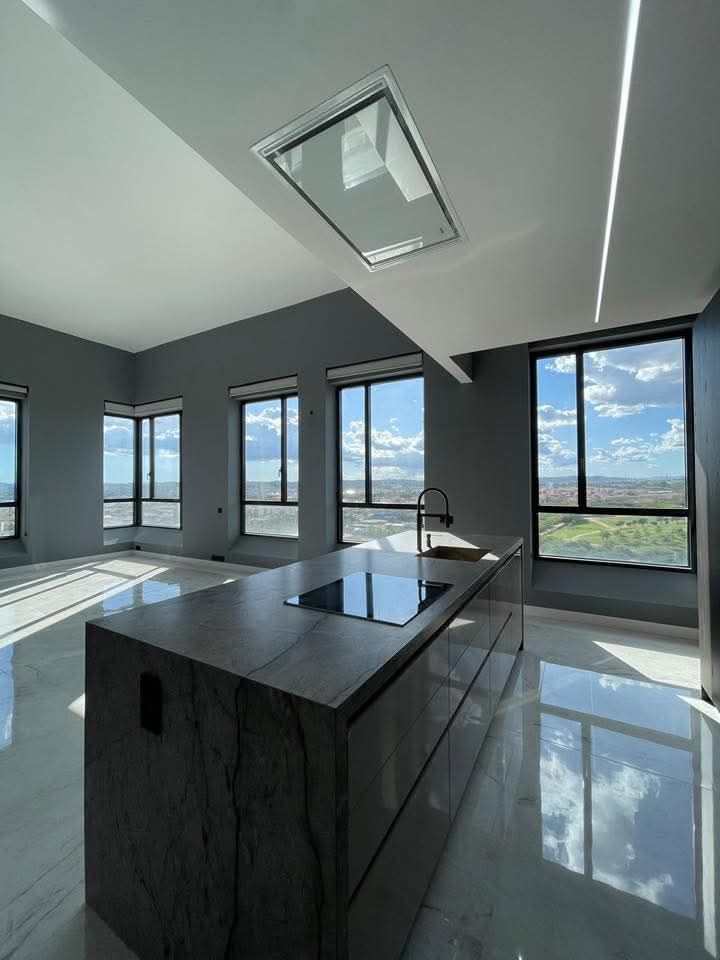 Cocina moderna con isla, amplios ventanales y vistas a la ciudad.