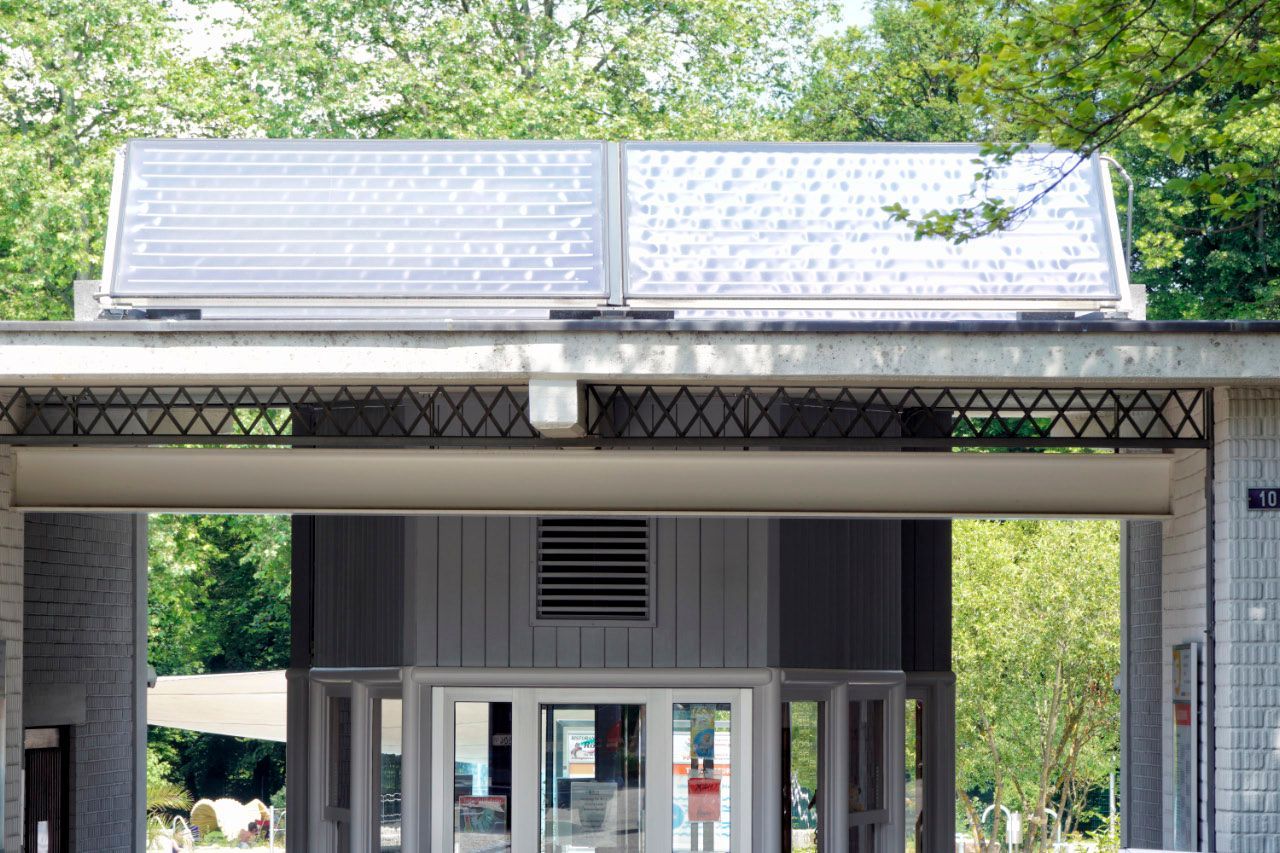 Solarmodule auf einem Gebäudedach mit einem Eingang und Bäumen im Hintergrund.