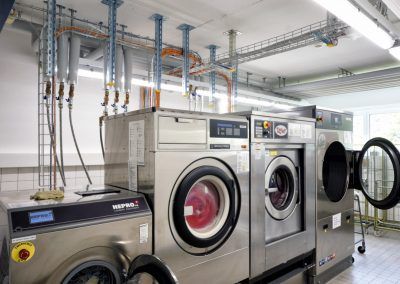 Reihe von Industriewaschmaschinen in einem hell erleuchteten Waschraum.