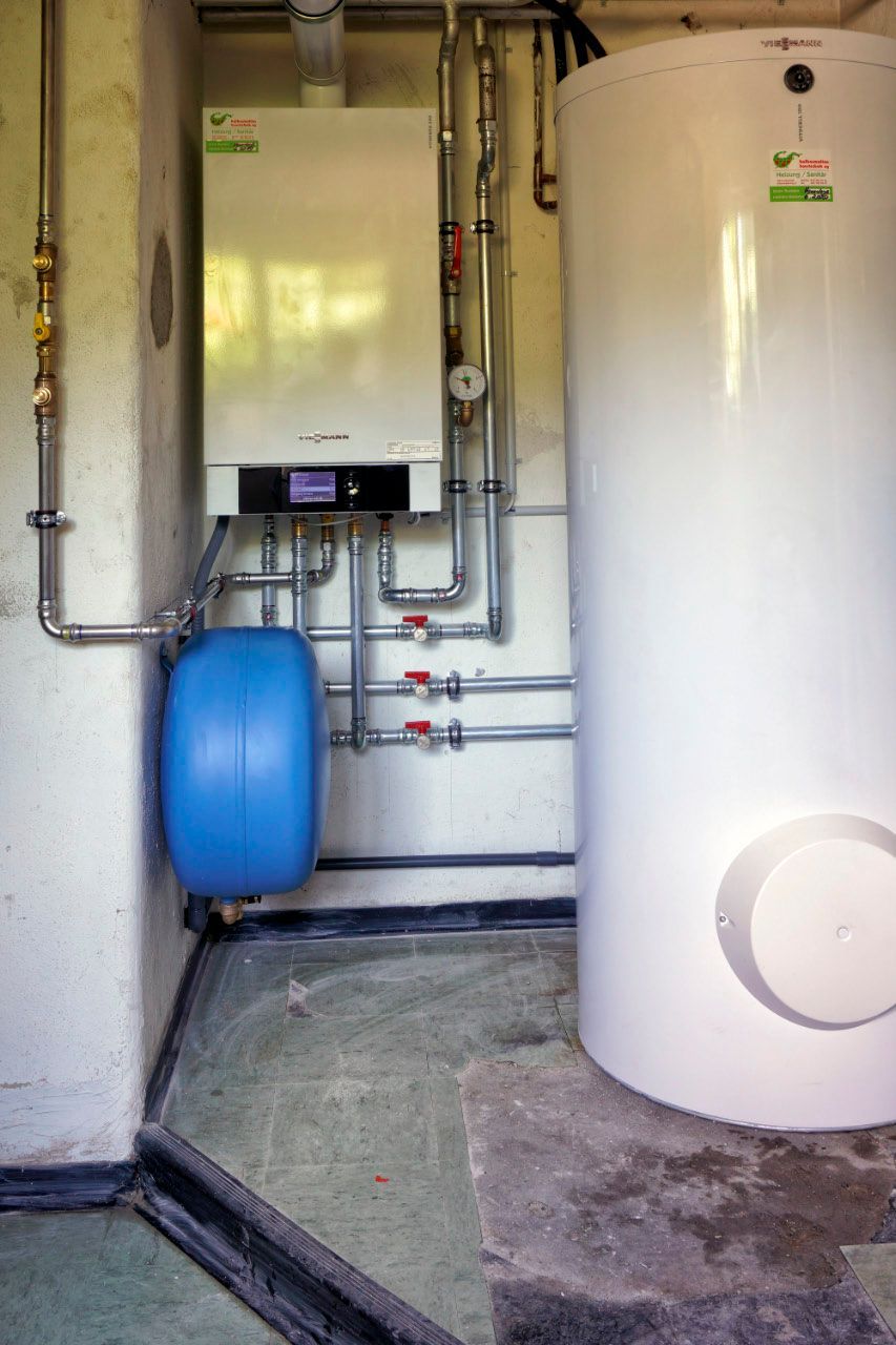 Heizsystem mit weißem Kessel, Tank, blauem Ausdehnungsgefäß und Rohren in einem Keller.