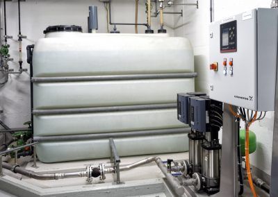Wassertank und Pumpanlage in einem Hauswirtschaftsraum, mit Bedienfeld und Sanitäranlagen.