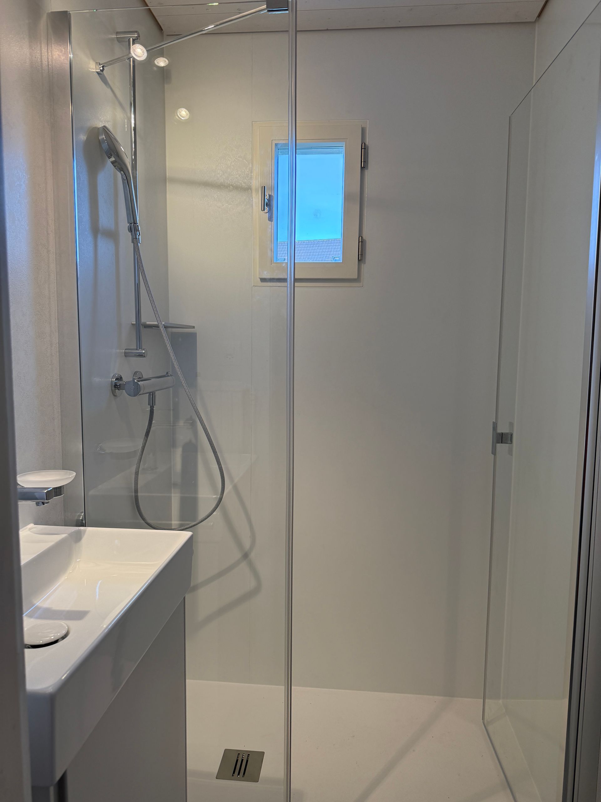 Modernes Badezimmer in Grau-Weiß-Farbgebung mit Dusche, Waschbecken und Toilette.