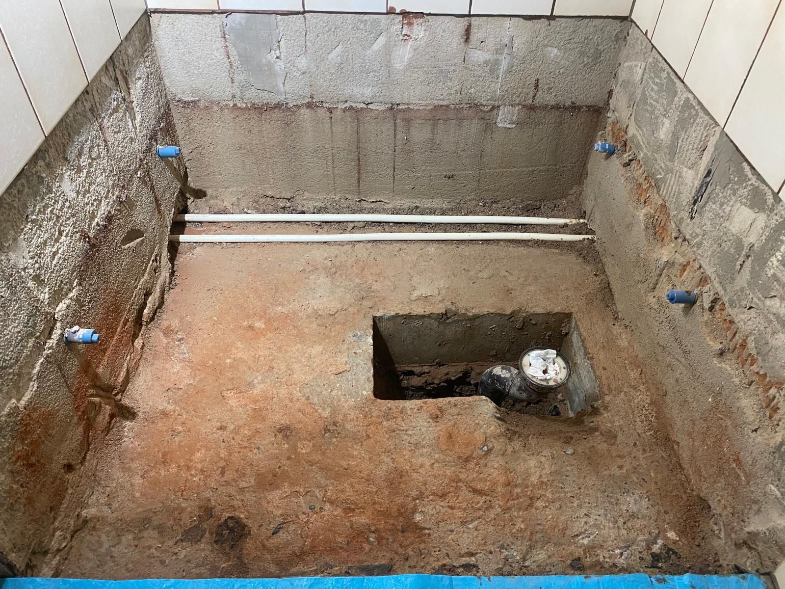 Mann in Overall und Mütze fliest eine Wand, Werkzeuge auf einem Tisch.