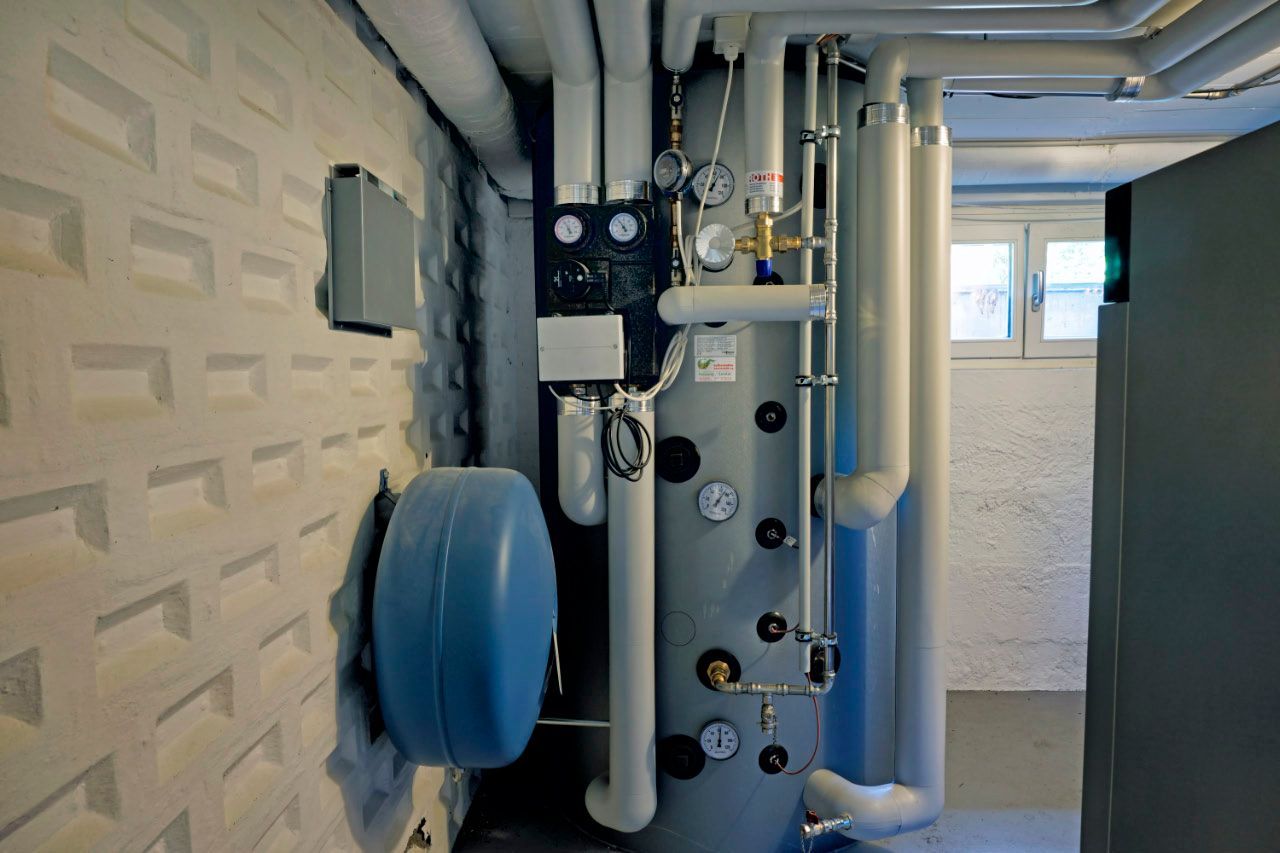 Ein Kellerraum mit einem großen silbernen Warmwasserbereiter und den dazugehörigen Rohren und Geräten.