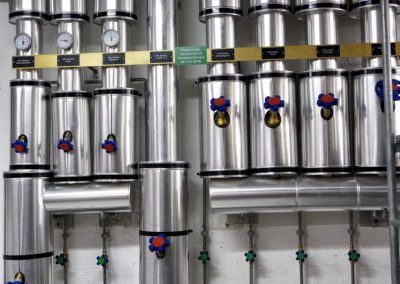 Silberne Rohre und Zylinder mit Messgeräten, Ventilen und Armaturen in einer industriellen Umgebung.