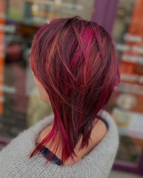 Une personne aux cheveux roux et orange ondulés et éclatants, coiffés de dos, photographiée dans un salon de coiffure.