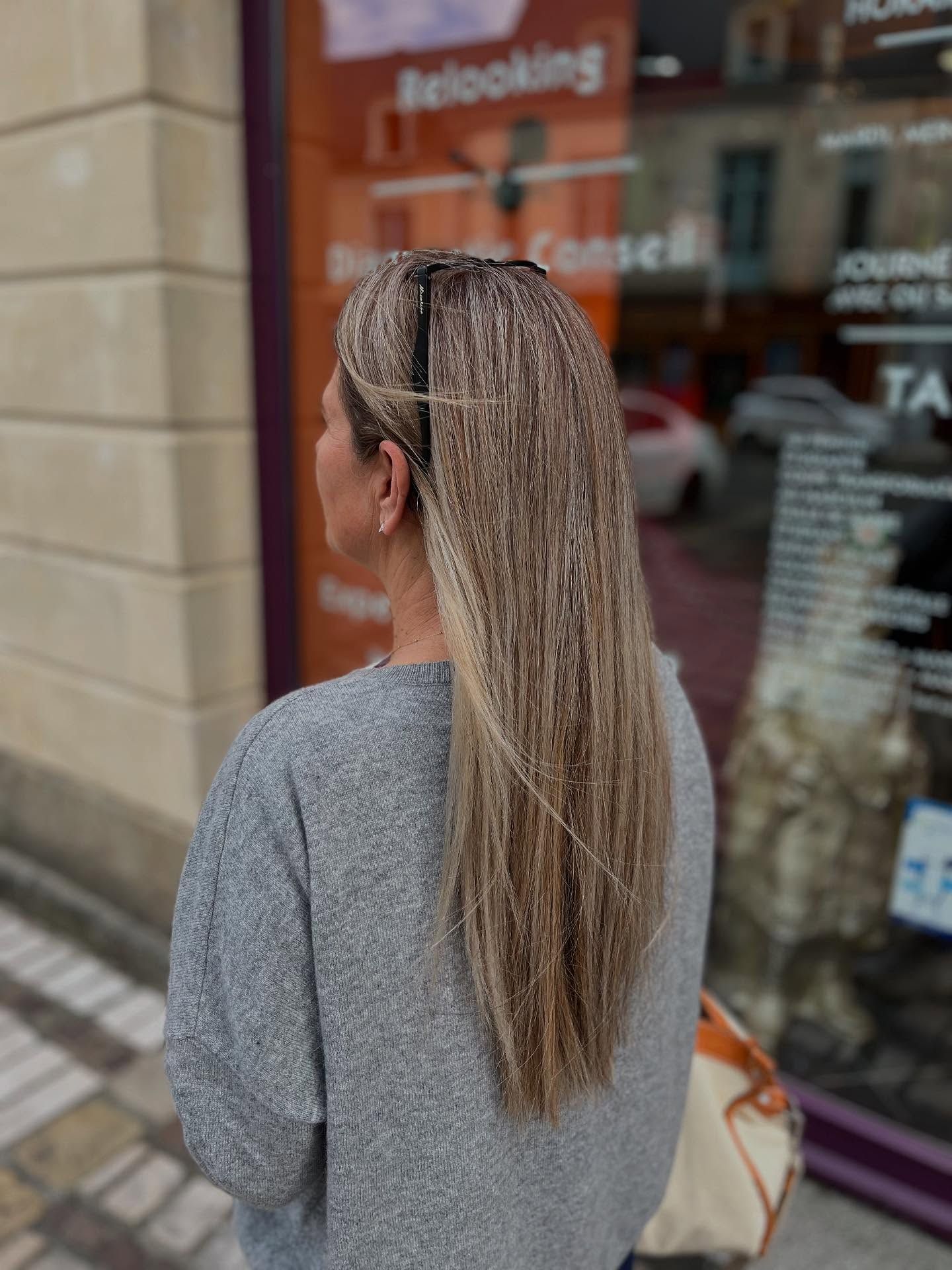 Une personne aux longs cheveux blonds et frisés, vue de dos, debout devant la vitrine d'un magasin.