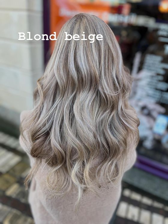 Une personne aux longs cheveux ondulés, avec des mèches blondes, lâchés, vue de dos, portant une chemise à rayures.