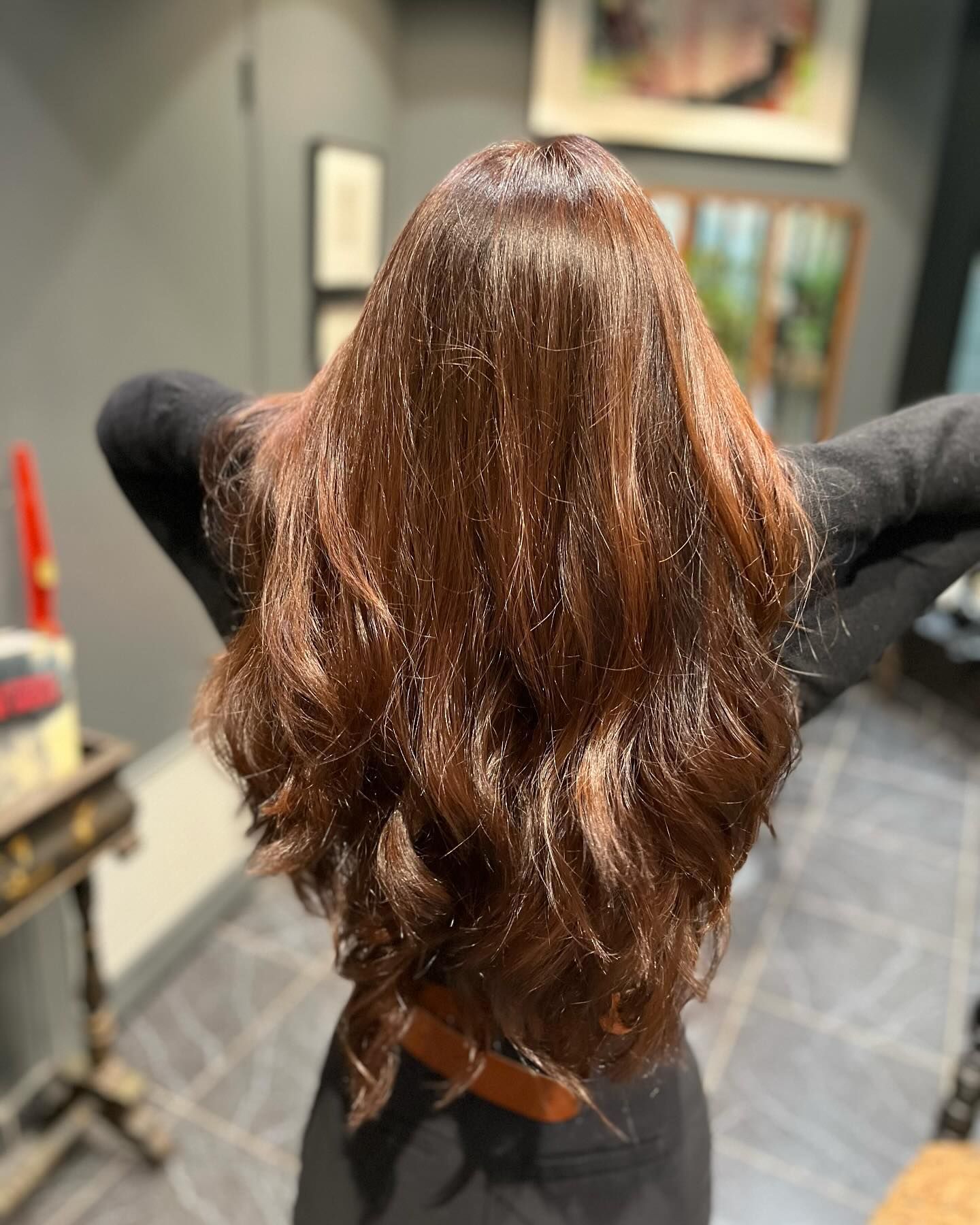 Vue de dos d'une personne aux longs cheveux bruns ondulés avec de subtils reflets, dans un salon de coiffure.