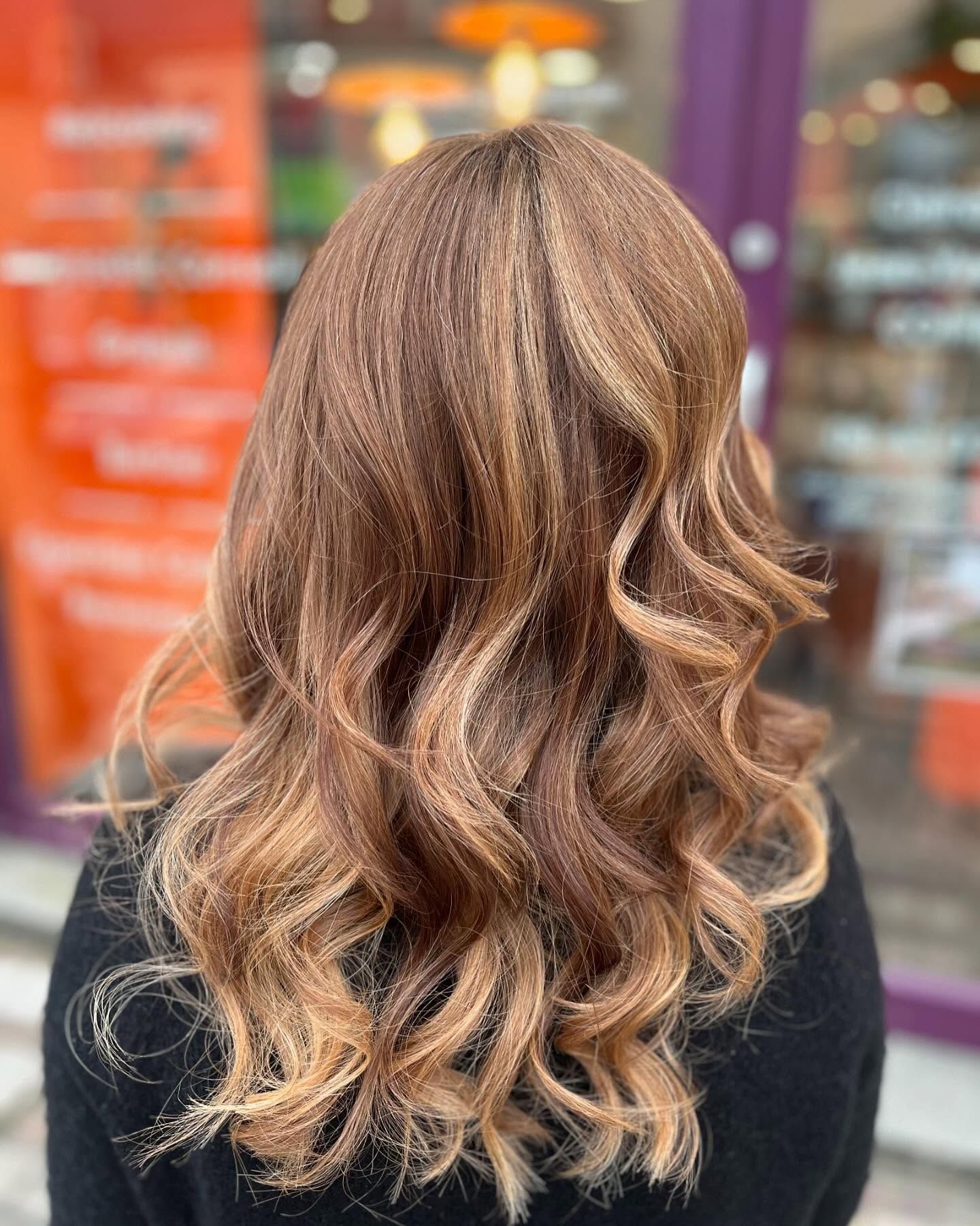 Une personne vue de dos, aux cheveux bruns ondulés mi-longs avec des reflets caramel plus clairs.