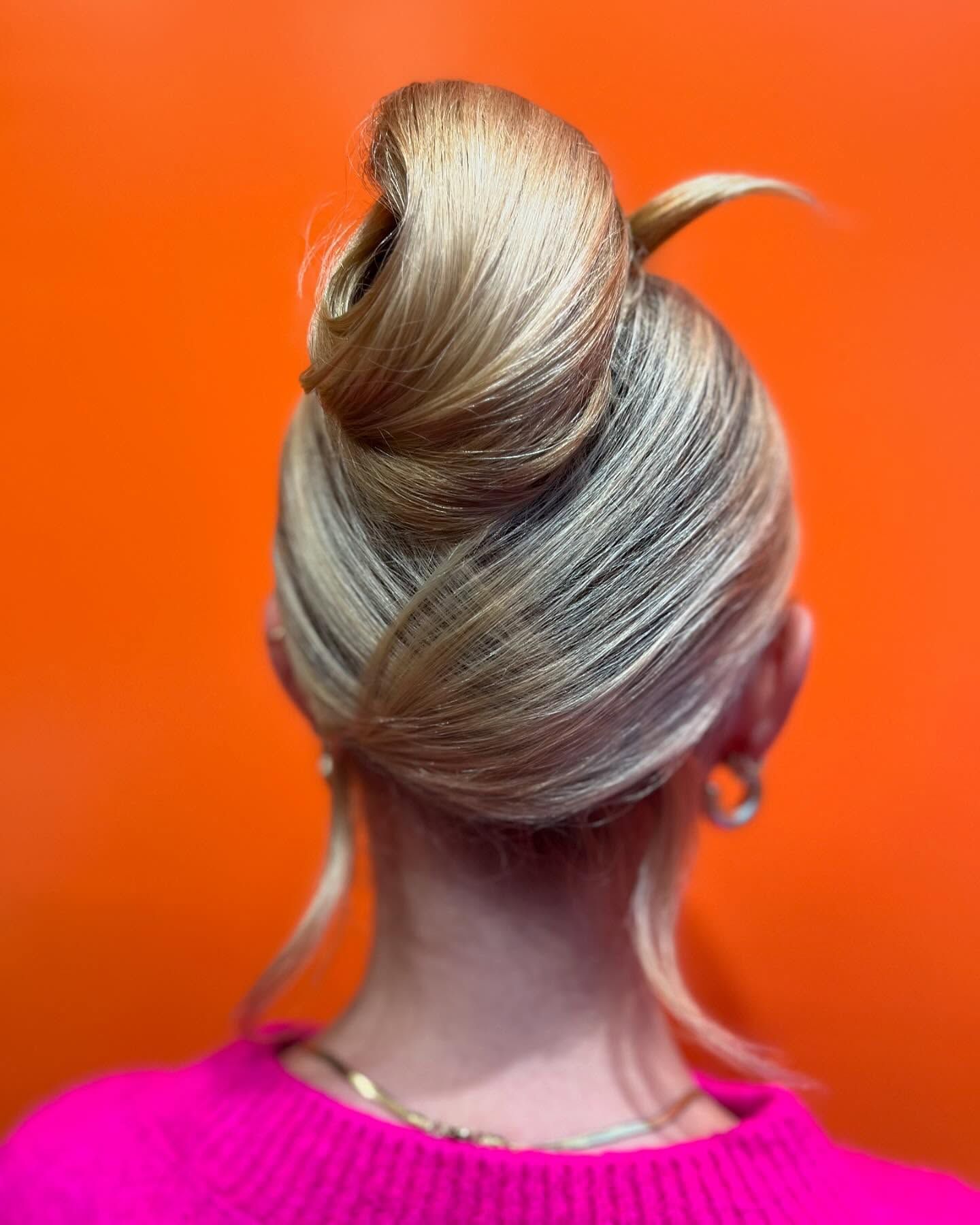 Une personne aux cheveux blonds et crêpés, coiffure structurée, sur un fond orange vif.