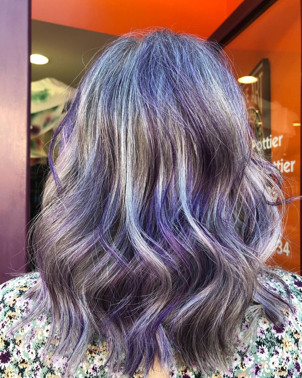 Cheveux ondulés mi-longs, coiffés de mèches aux tons violet vif, argent glacé et gris anthracite foncé.