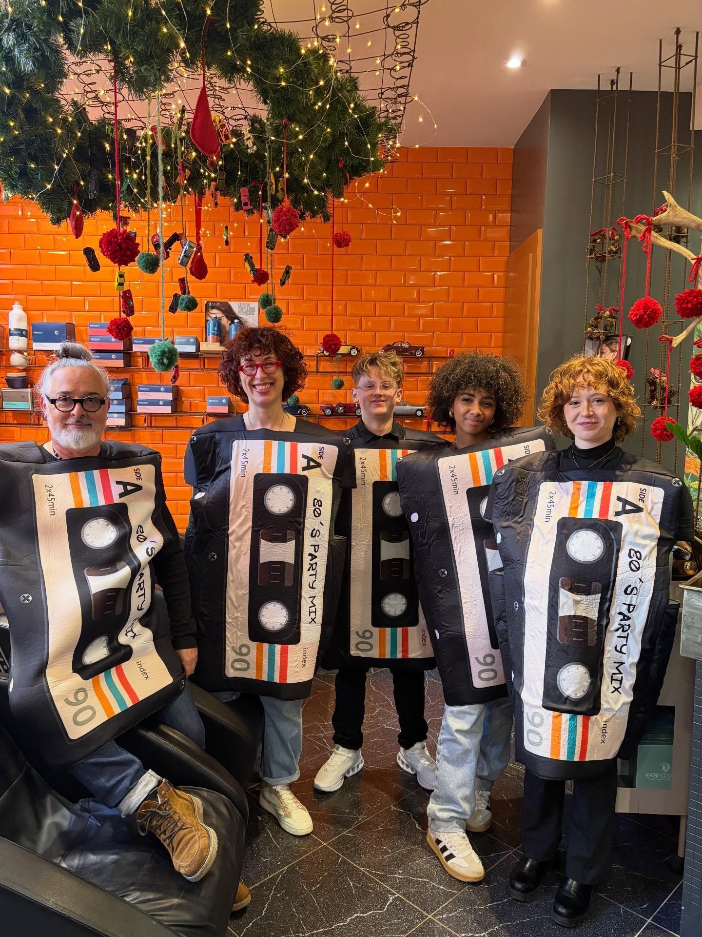 Cinq personnes dans un magasin, vêtues de costumes assortis en forme de cassettes audio, pour un événement festif devant des murs de briques orange.
