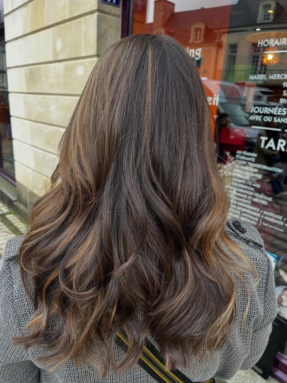 Une personne aux longs cheveux ondulés avec des mèches brunes, vue de dos, debout devant la vitrine d'un magasin.
