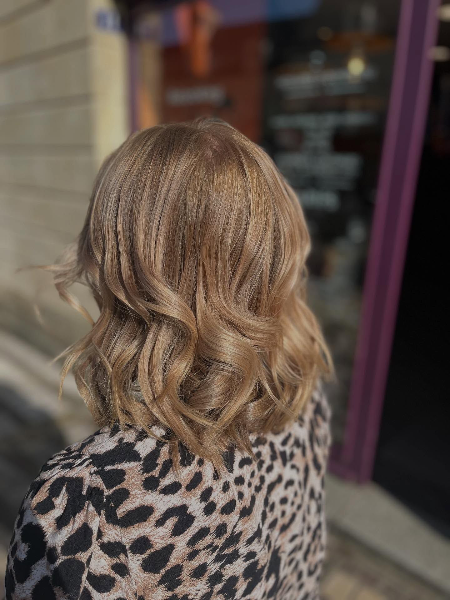 Une personne aux cheveux châtain clair mi-longs, coiffés en ondulations souples et légèrement crêpés, portant un haut à imprimé léopard.
