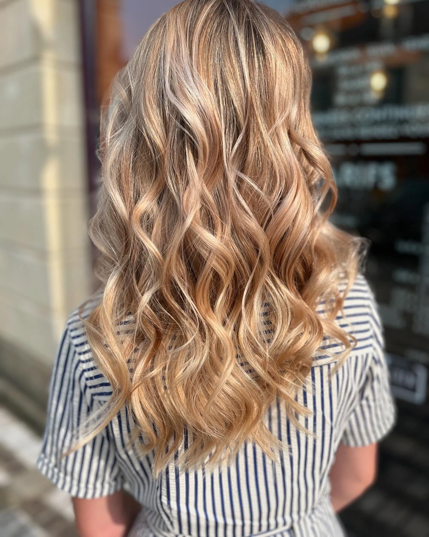 De dos, une personne aux longs cheveux blonds ondulés et méchés, vêtue d'une chemise à rayures, se tient devant la vitrine d'un magasin.