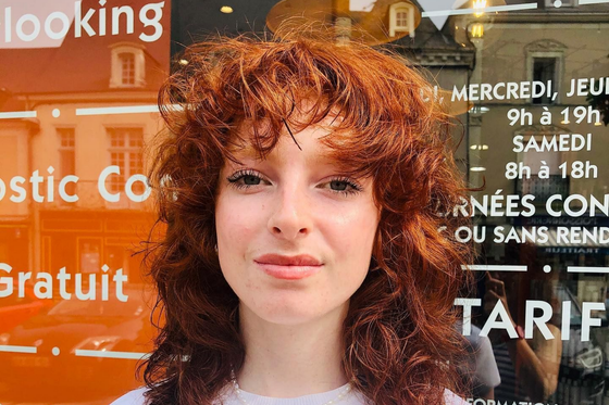 Une personne portant un pull rose vif, vue de dos, avec une coupe au carré blonde lisse arrivant aux épaules.