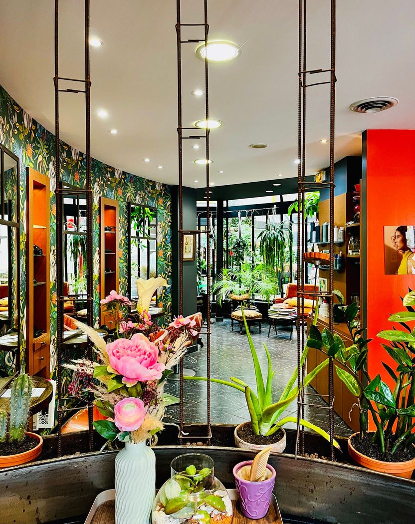 Une pièce avec du papier peint à motifs, des plantes et une décoration colorée, que l'on aperçoit à travers un paravent décoratif en métal.