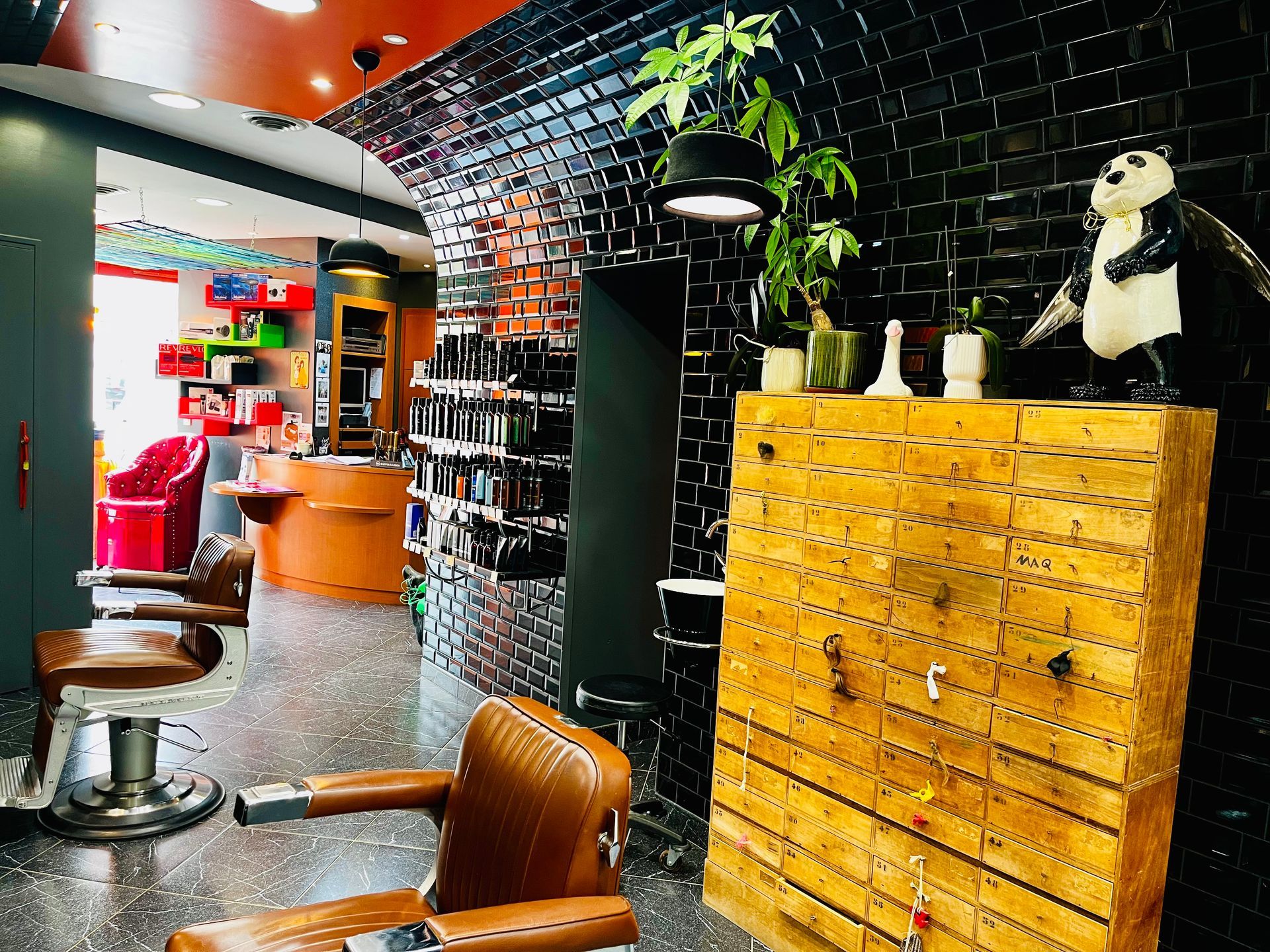 L'intérieur d'un salon de coiffure avec des fauteuils en cuir, une armoire en bois, des murs carrelés noirs et une statue de panda.