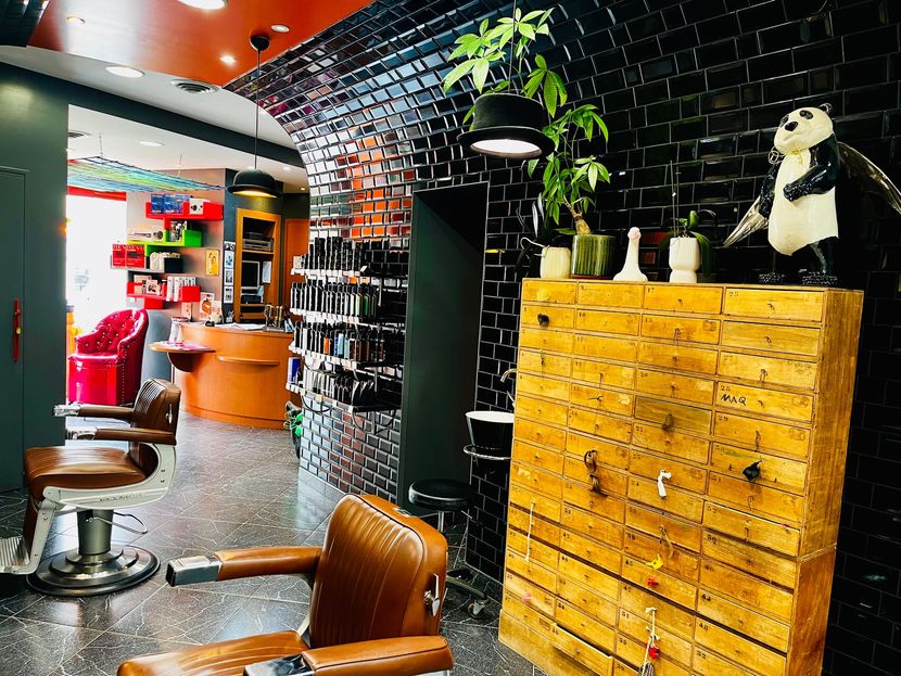 L'intérieur d'un salon de coiffure avec des fauteuils en cuir, une armoire en bois, des murs carrelés noirs et une statue de panda.