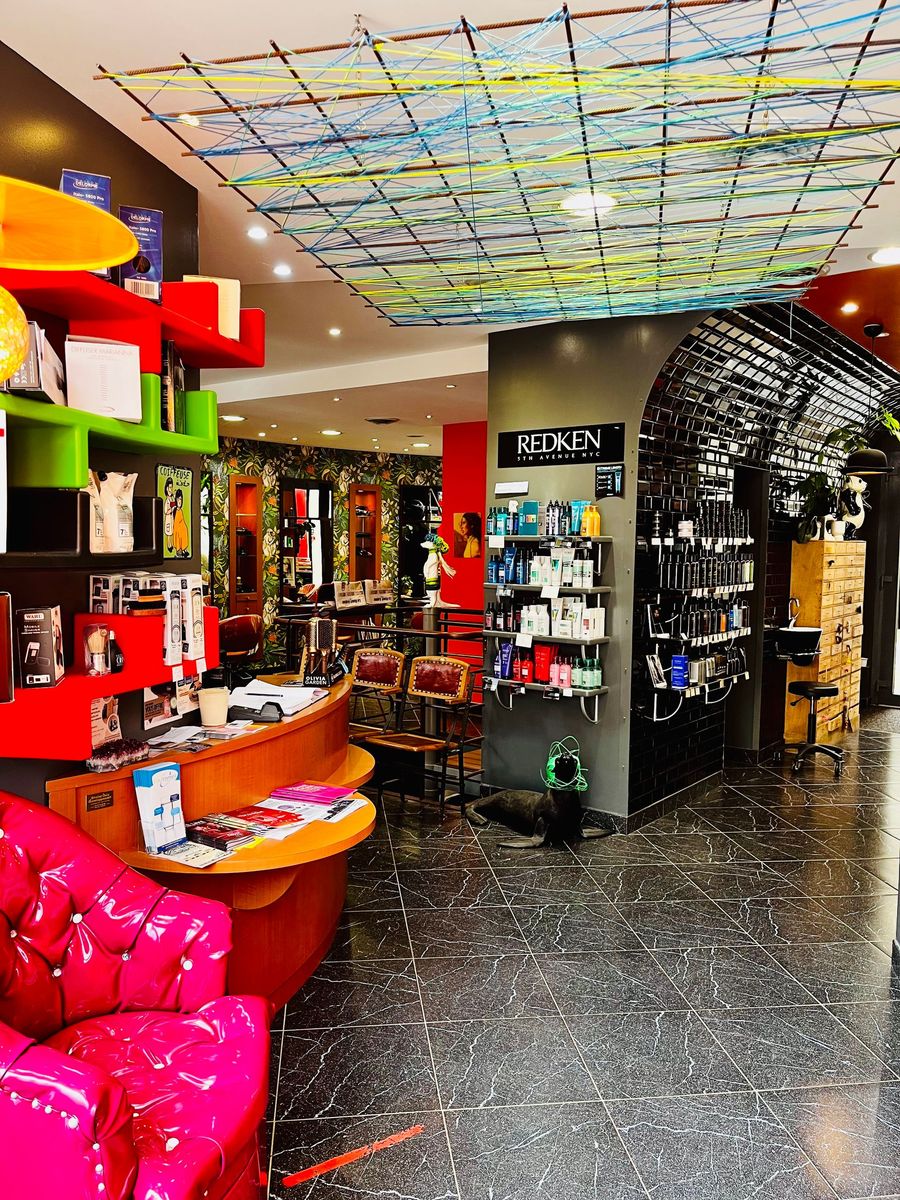 Intérieur de salon moderne avec un fauteuil rose vif, des étagères colorées, des produits exposés et un plafond à motifs.