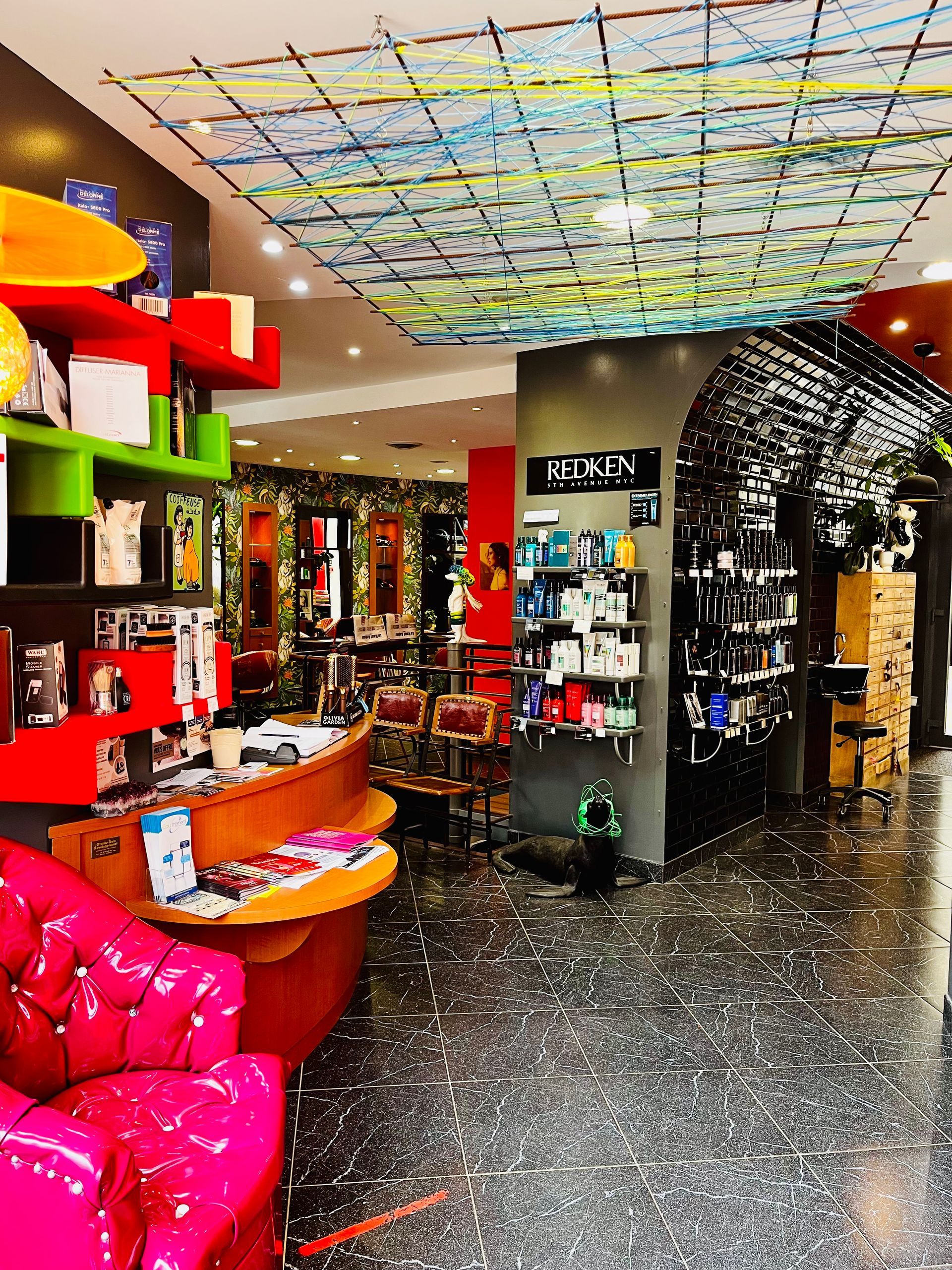 Intérieur de salon moderne avec un fauteuil rose vif, des étagères colorées, des produits exposés et un plafond à motifs.
