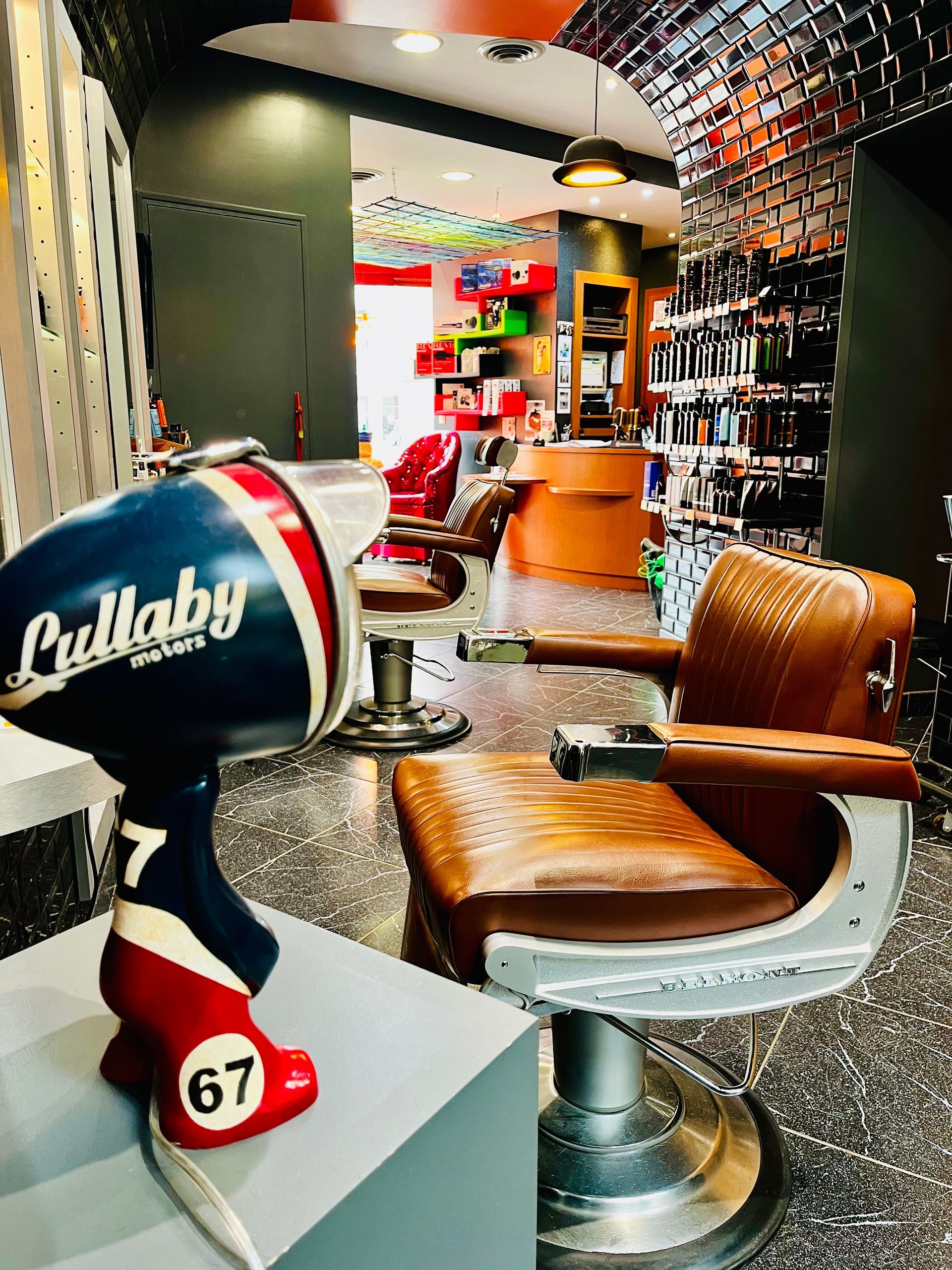 Dans un salon de coiffure, un sèche-cheveux vintage à motifs en forme de casque de voiture de course est posé à côté d'un fauteuil de barbier en cuir marron.