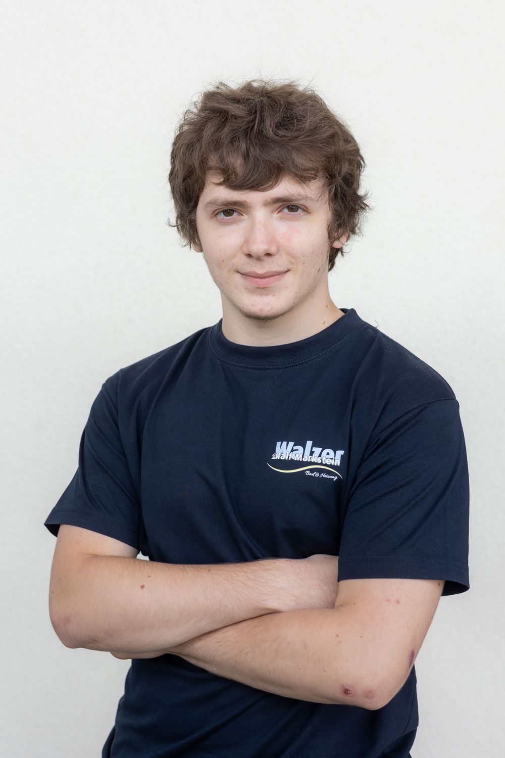 Eine lächelnde Person in einem leuchtend gelben Poloshirt steht drinnen in der Nähe eines Fensters.