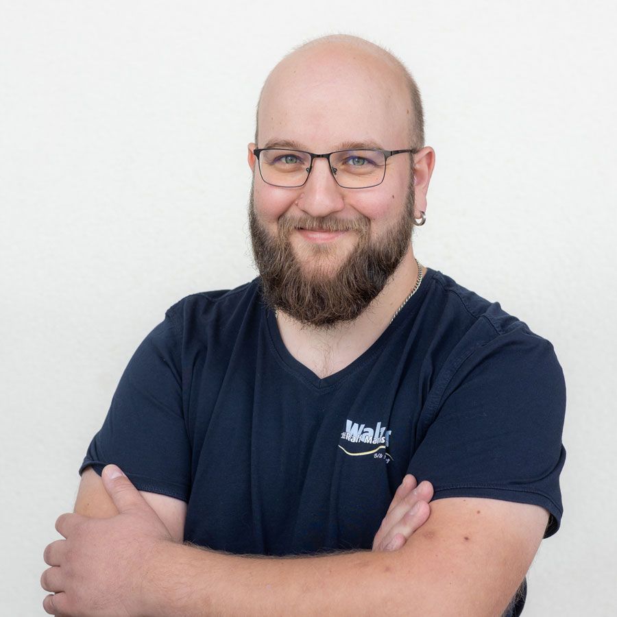 Mann in einem gelben Poloshirt mit verschränkten Armen, der vor einer beigen Wand steht.