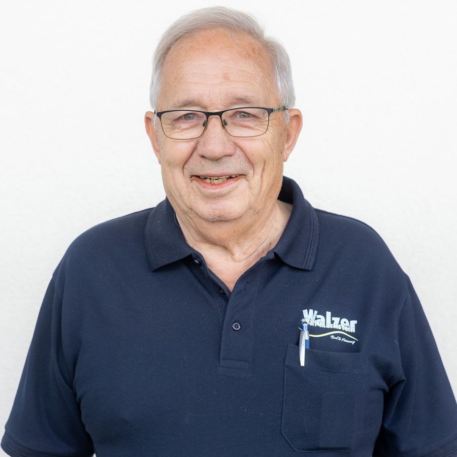 Eine Person mit Brille und Armbanduhr steht mit verschränkten Armen drinnen vor einer beigen Wand.