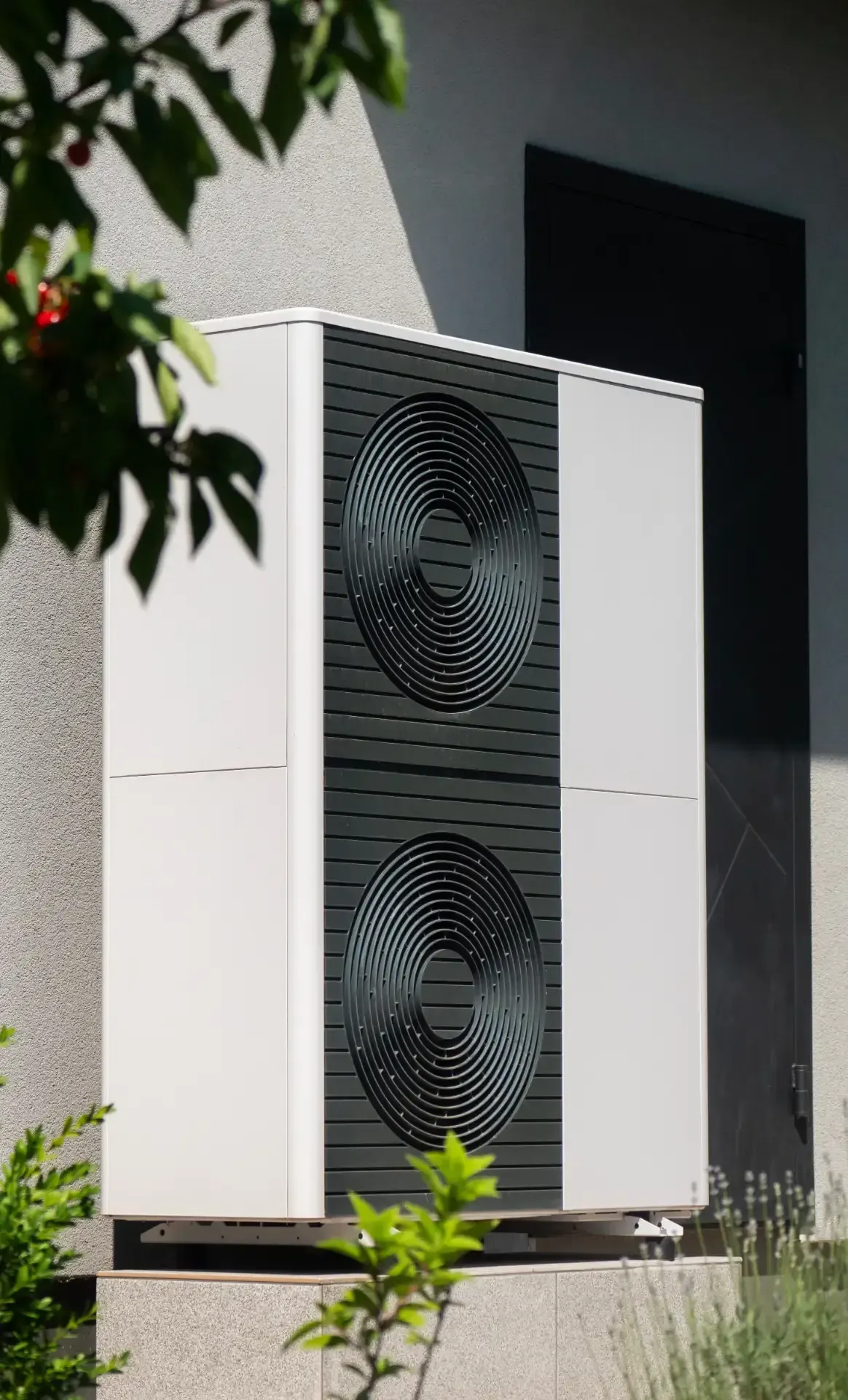 Weiße Außeneinheit der Wärmepumpe mit zwei schwarzen Ventilatoren neben einer Gebäudewand
