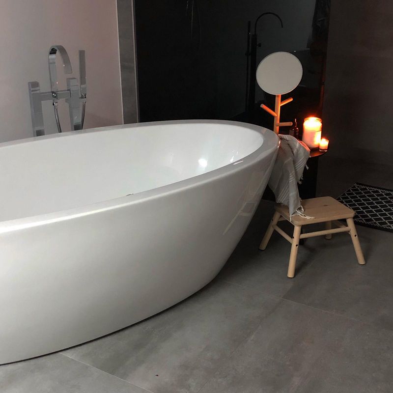 Modernes Badezimmer mit freistehender weißer Badewanne, Hocker und brennenden Kerzen in einer dunklen Ecke