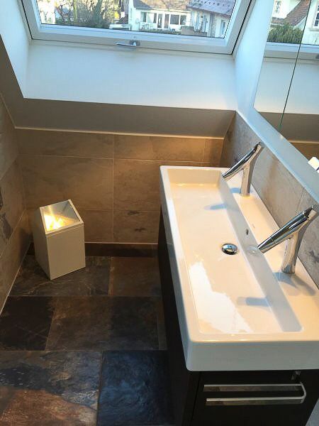 Modernes Badezimmer mit weißem Waschbecken, wandmontierter Armatur, dunklem Fliesenboden und Fensternische