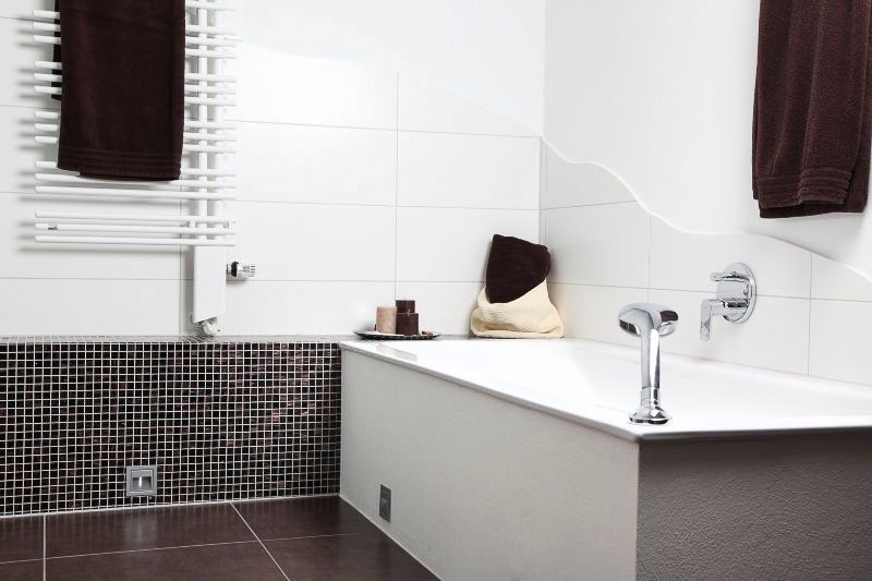 Modernes weißes Badezimmer mit gefliesten Wänden, Badewanne und dunkelbraunen Akzenten