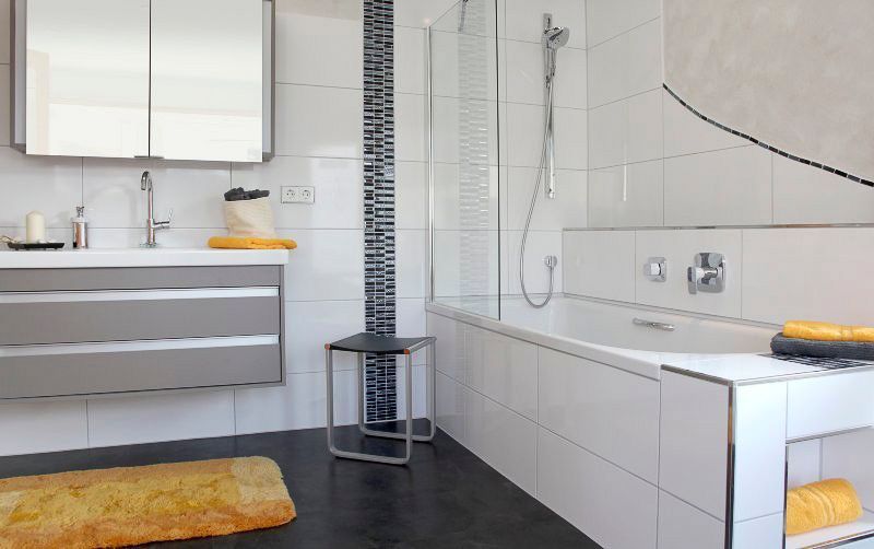 Modernes Badezimmer mit grauem Waschtisch, weißer Badewanne, schwarzem Boden und gelben Handtüchern.