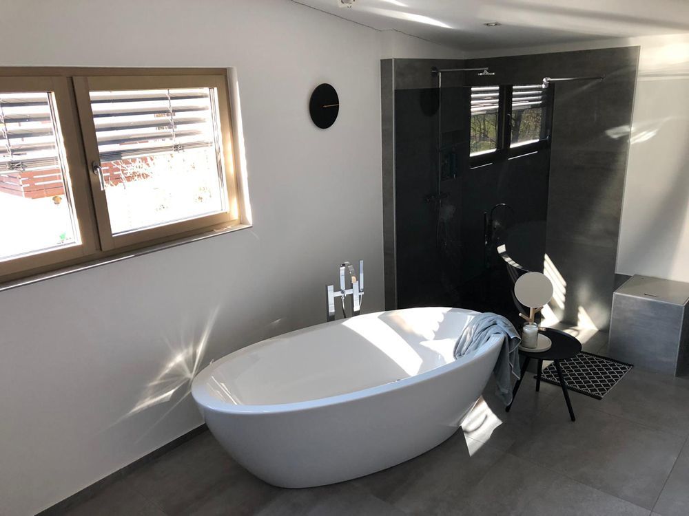 Modernes Badezimmer mit freistehender Badewanne, schwarzer Duschkabine und Tageslicht durch die Fenster