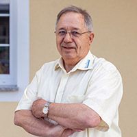 Eine Person mit Brille und Armbanduhr steht mit verschränkten Armen drinnen vor einer beigen Wand.