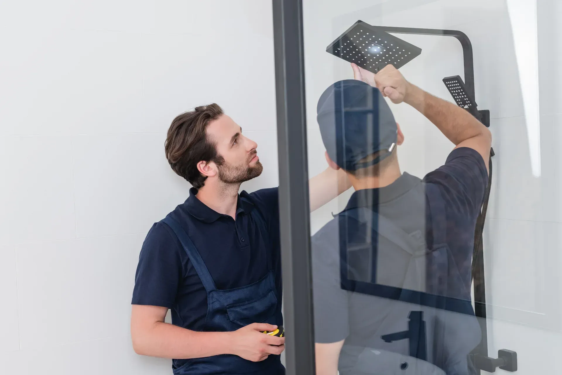 Zwei Personen justieren eine schwarze Wandleuchte in einer Duschkabine aus Glas.