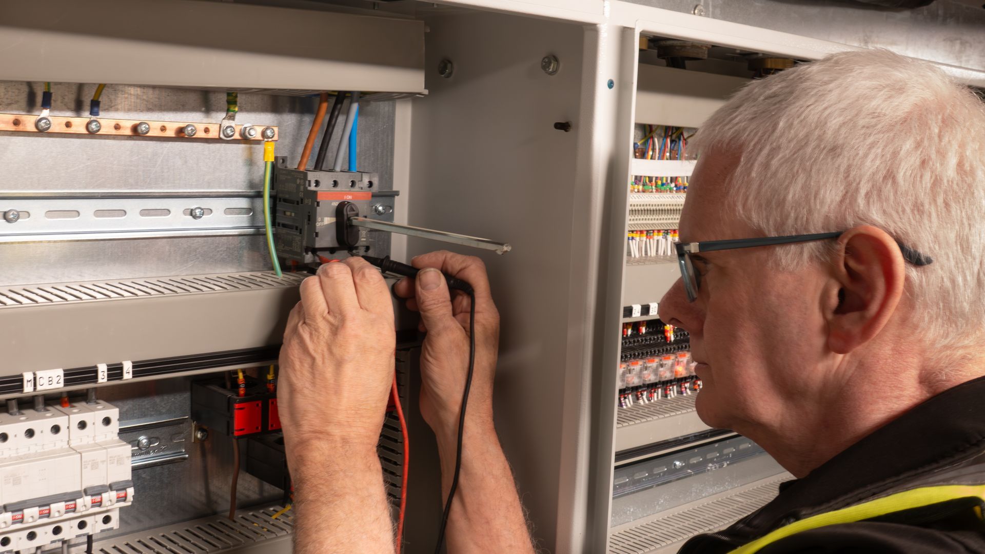 Un technicien effectue le câblage d'un panneau de commande électrique à l'aide de câbles à l'intérieur d'une armoire ouverte.