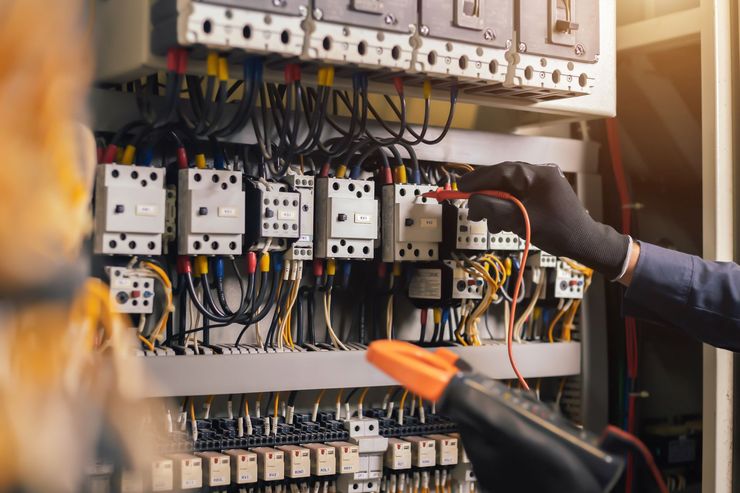 Un électricien inspecte un tableau électrique encombré de fils, de disjoncteurs et d'outils.