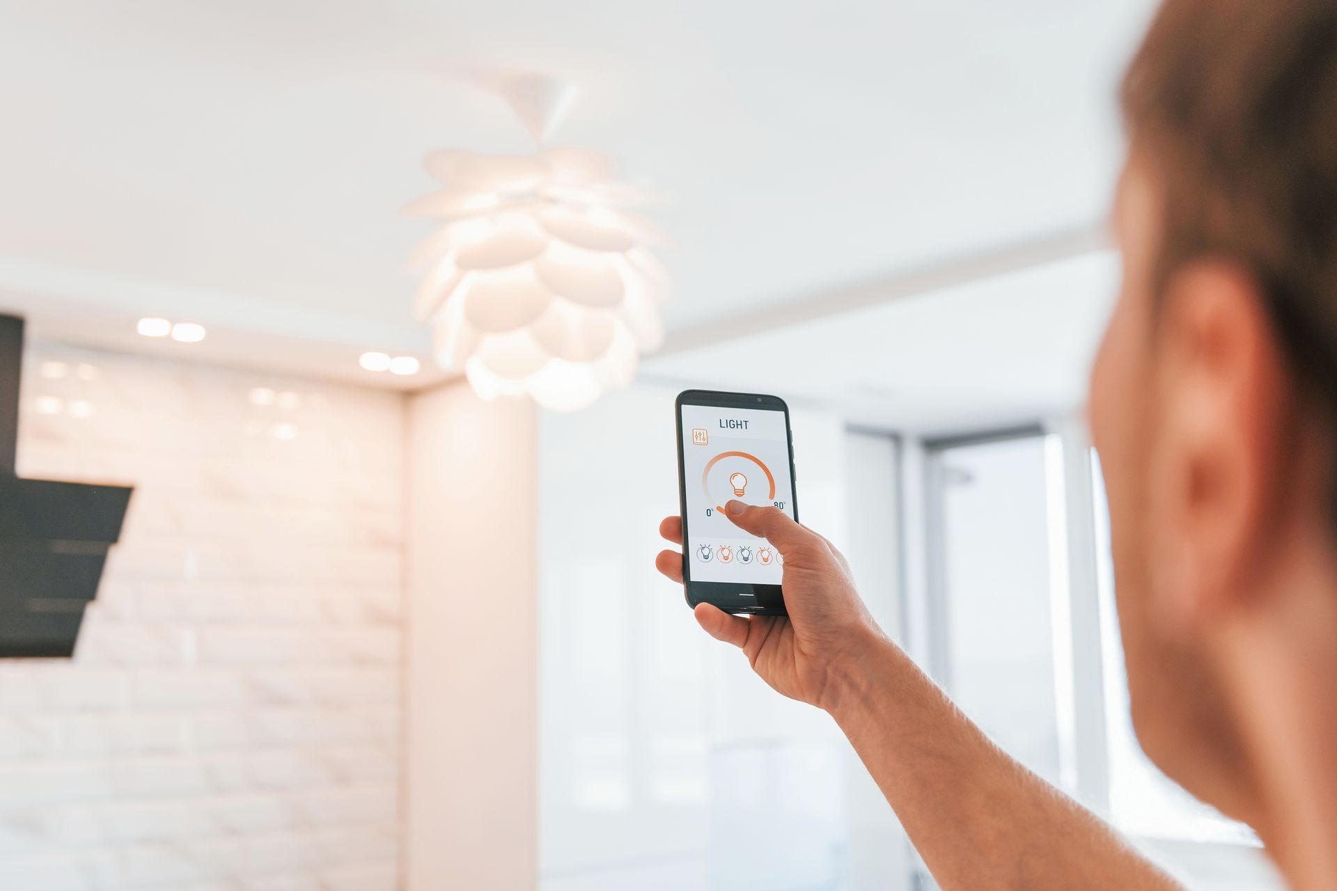 Une personne utilise un smartphone pour contrôler un plafonnier dans une cuisine moderne et lumineuse.