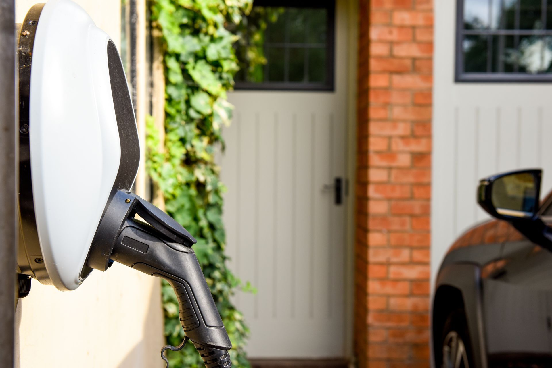 Recharge d'une voiture électrique dans une allée privée, à côté d'un garage et d'un véhicule stationné.